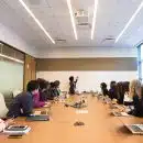 people on conference table looking at talking woman